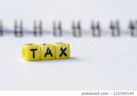 TAX text on colorful plastic alphabet beads with blurred notepad background TAX text on colorful plastic alphabet beads with blurred notepad background 122500144