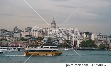 Scenic View of Istanbul's Galata Tower and Cityscape from the Water with a Yellow Passenger Ferry Boat 122500678