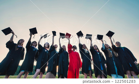 Group of cheerful students wearing academic gowns raising mortarboards in the air celebrating their graduation day Group of cheerful students wearing academic gowns raising mortarboards in the air celebrating their graduation day 122501283