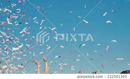 High school graduates joyfully tossing vibrant confetti into the air on a sunny summer day 122501303