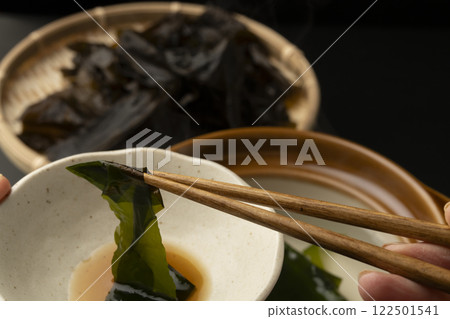 Eating raw wakame seaweed shabu-shabu. Picking up the raw wakame seaweed with chopsticks. 122501541
