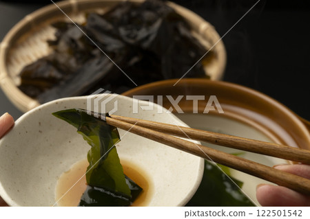 Eating raw wakame seaweed shabu-shabu. Picking up the raw wakame seaweed with chopsticks. 122501542