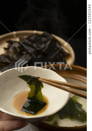 Eating raw wakame seaweed shabu-shabu. Picking up the raw wakame seaweed with chopsticks. Eating raw wakame seaweed shabu-shabu. Picking up the raw wakame seaweed with chopsticks. 122501543