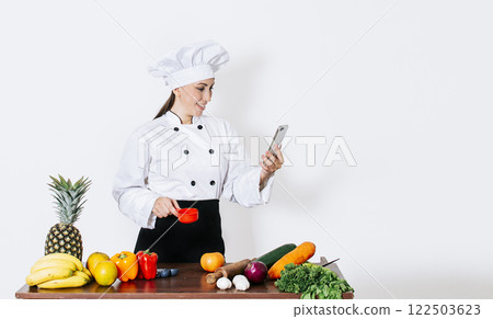 Woman chef with vegetables on the table looking for recipes with her smartphone. A woman chef in the kitchen looking for recipes with her cell phone, Chef people looking for cooking recipes Woman chef with vegetables on the table looking for recipes with her smartphone. A woman chef in the kitchen looking for recipes with her cell phone, Chef people looking for cooking recipes 122503623