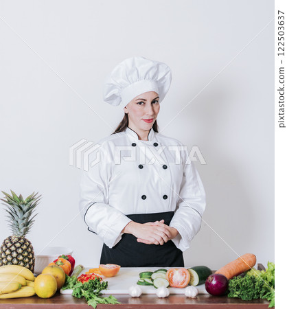 Portrait of a female chef surrounded by fresh vegetables, Portrait of a female chef with fresh vegetables on the table, A female nutritionist with a table of vegetables Portrait of a female chef surrounded by fresh vegetables, Portrait of a female chef with fresh vegetables on the table, A female nutritionist with a table of vegetables 122503637