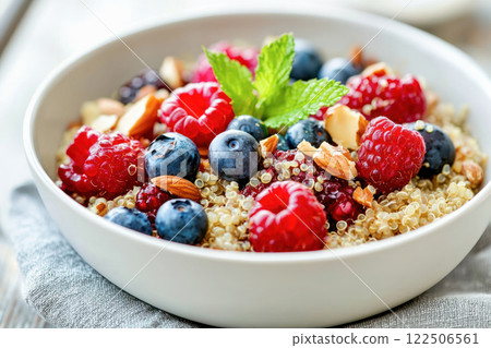 Close-up of a quinoa breakfast bowl topped with fresh berries, almonds, and mint on a soft fabric napkin. 122506561