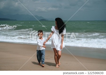Happy mom and son walking along beach by the sea on summer vacation 122506630