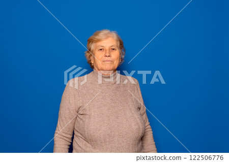 Horizontal portrait of a Caucasian woman in her 70s posing proudly and satisfied with the stage of her life she is living, isolated on a blue studio background. 122506776