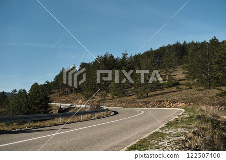 Automobile rural paved empty road meanders along a green coniferous forest on a sunny summer day. The nature of southwestern Serbia near Zlatibor town in early autumn 122507400
