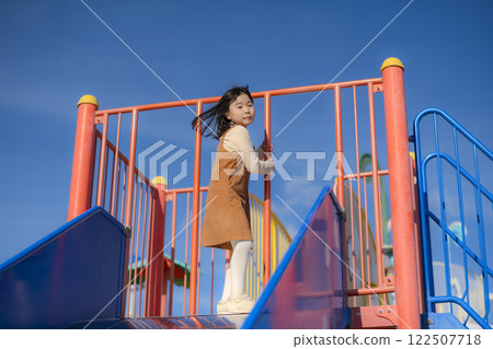 Cheerful girl playing on a slide in the park Cheerful girl playing on a slide in the park 122507718