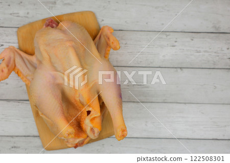 Close-up top view of a butchered raw chicken lying on a wooden cutting board against a white wood background with space for text. The concept of cooking, diet menu, ingredients. High quality photo 122508301