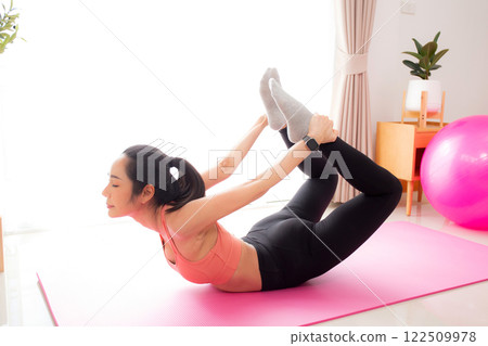 Young asian woman practicing Yoga with stretching muscle back on yoga mat in living room at home. Young asian woman practicing Yoga with stretching muscle back on yoga mat in living room at home. 122509978