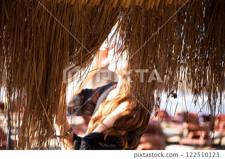 Woman under thatched beach umbrella adjusting sunglasses in sunlight  122510123