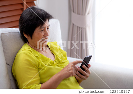 Senior asian woman sitting on sofa looking smartphone for video call in living room at home. 122510137