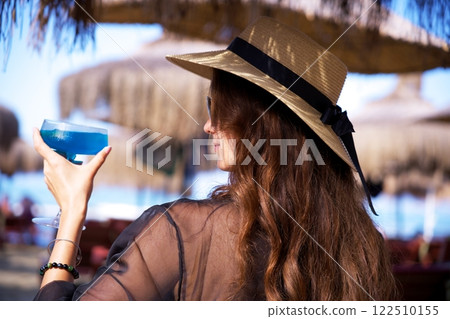 Elegant woman holding blue cocktail at tropical beach resort Elegant woman holding blue cocktail at tropical beach resort 122510155