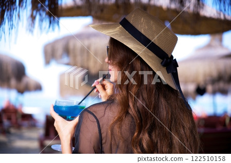 Woman in straw hat sipping blue cocktail at tropical beach resort Woman in straw hat sipping blue cocktail at tropical beach resort 122510158