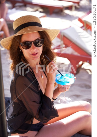 Elegant woman in sun hat enjoying tropical blue cocktail Elegant woman in sun hat enjoying tropical blue cocktail 122510171