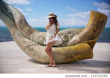 Elegant woman posing on artistic seaside sculpture Elegant woman posing on artistic seaside sculpture 122510189