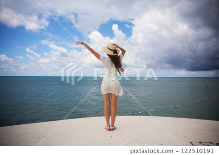 Carefree woman with sun hat embracing ocean breeze  122510191