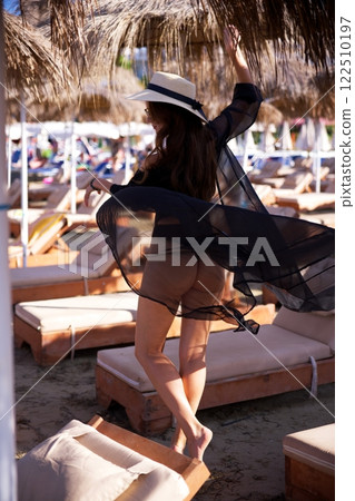 Elegant woman in sheer beach cover-up twirling  122510197