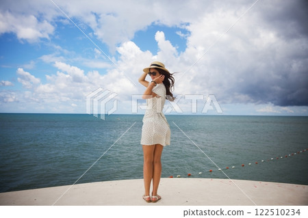 Woman in sun hat enjoying ocean breeze on seaside platform Woman in sun hat enjoying ocean breeze on seaside platform 122510234