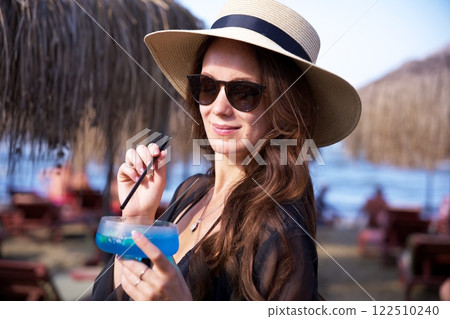 Elegant woman enjoys blue cocktail at beach resort  122510240