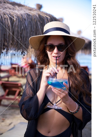Chic woman sipping a cold blue cocktail at beach Chic woman sipping a cold blue cocktail at beach 122510241