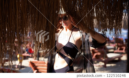 Woman in black bikini under tropical thatched umbrella on sandy beach Woman in black bikini under tropical thatched umbrella on sandy beach 122510246