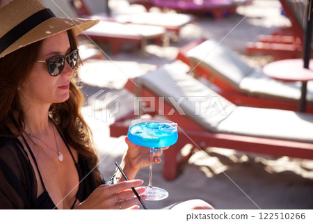 Elegant woman sipping blue cocktail at tropical beach Elegant woman sipping blue cocktail at tropical beach 122510266