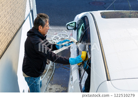A man washing his car in his home parking lot A man washing his car in his home parking lot 122510279