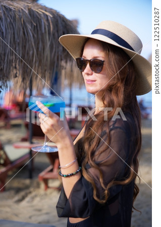 Chic woman in sun hat holding blue tropical cocktail  122510287