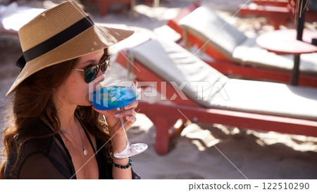 Stylish woman enjoying a refreshing blue cocktail on beach  122510290