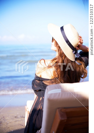 Elegant woman relaxing by the ocean in summer sunshine Elegant woman relaxing by the ocean in summer sunshine 122510317