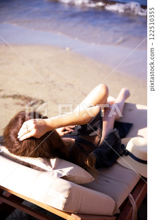 Woman relaxing on beach lounge by the shore  122510355