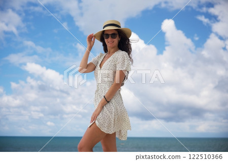 Smiling woman in sun hat enjoying ocean breeze under blue sky Smiling woman in sun hat enjoying ocean breeze under blue sky 122510366