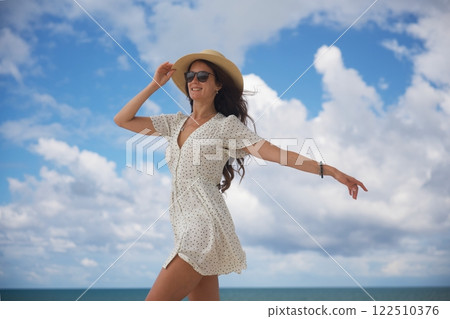 Joyful woman in sun hat dancing by the ocean  122510376