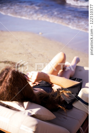 Woman lounging on beach chair by the sea Woman lounging on beach chair by the sea 122510377