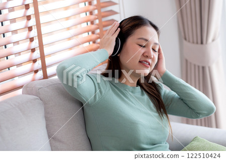Happy young asian woman wearing headphones listening music while sitting on sofa with fun and enjoy. Happy young asian woman wearing headphones listening music while sitting on sofa with fun and enjoy. 122510424
