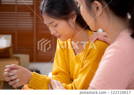 Young asian woman comforting friend with crying and depression sitting on sofa in living room. 122510617
