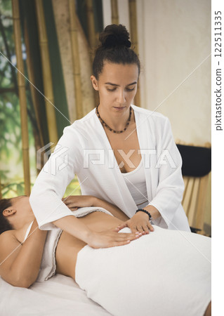 Female therapist massages the internal organs through the clients abdomen in pro salon, vertical format, selective focus. 122511335