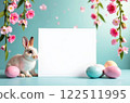 A white square for text in the center of the picture, a light rabbit is sitting next to it and Easter eggs of different colors are lying, pink flowers hanging on top on a blue background. The concept 122511995