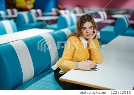 Young woman in yellow sweater enjoying coffee in a colorful cafe 122512918