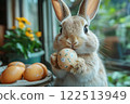 Easter Bunny in room holds painted egg in its paws. 122513949