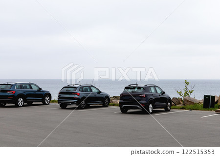 Parked cars on the seashore. Rocky seashore and houses in cloudy weather. 122515353