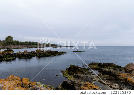 Coast line of sea. Stones covered with yellow and green moss and cloudy sky. 122515370
