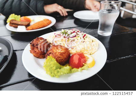 Seafood restaurant on the seashore. White plate with fish patties, fish fillets and potato salad. 122515457
