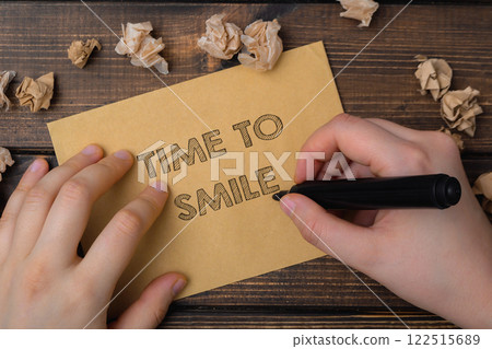 Hand is writing on a piece of paper that says Time to smile. 122515689