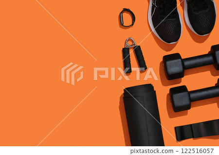 Black exercise equipment, dumbbells, mat, elastic band, fitness band, fitness band, sneakers on orange background. Fitness, sports items, healthy lifestyle. Place for your text 122516057