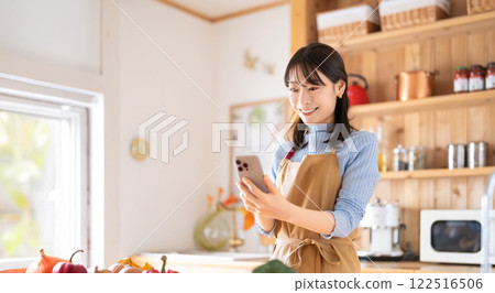 Smiling woman using smartphone in the kitchen Smiling woman using smartphone in the kitchen 122516506