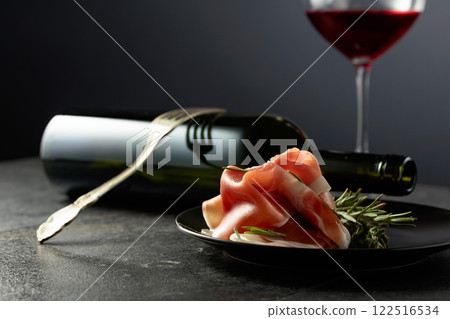 Prosciutto with rosemary and red wine on a black background. Prosciutto with rosemary and red wine on a black background. 122516534